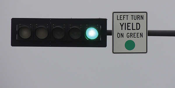 Figure 13. A picture of a 'LEFT TURN YIELD ON GREEN BALL' (MUTCD 10-12) sign on a signal mast arm adjacent to the left-turn signal head, which also shows a green ball display.