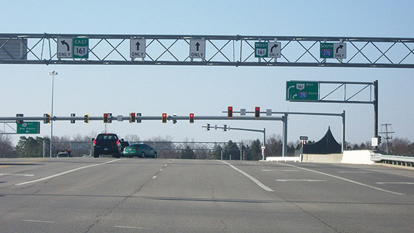 Figure 23. A picture of a five-lane approach to a signalized intersection at which an advance mast arm has been installed that displays lane-use control signs. Above the left lane is a left-turn-only Mandatory Movement Lane Control (R3-5) sign and a white-on-green guide sign for East Ohio Highway 161. Above the next two lanes are through-only Mandatory Movement Lane Control (R3-5a) signs. Above the two lanes on the right are right-turn-only Mandatory Movement Lane Control (R3-5R) signs; above the rightmo