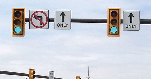Figure 24. A picture of two traffic signal heads mounted on a mast arm. Both signal heads have a yellow retroreflective strip around their outer borders. To the right of both signal heads is a through-only Mandatory Movement Lane Control (R3-5a) sign; a symbolic no-left-turn (R3-2) sign is next to the signal head on the left.