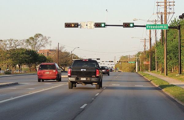 Figure 35. An image showing the approach to a signalized intersection with a mast arm-mounted signal head above each of the three approach lanes. The signal heads above the two through lanes show a green ball, and the signal head above the left-turn lane shows an active flashing yellow arrow for permissive left turns.