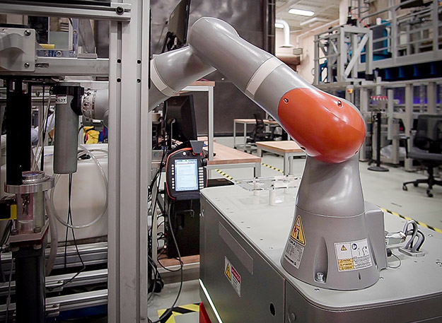 "This photograph shows the arm of an industrial robot reaching out with a soil sample in a Shelby tube preparing to insert it into the ESTD."