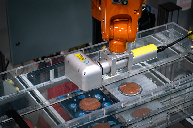 "the arm of the industrial robot positioning a laser scanner over the soil sample in the ESTD."