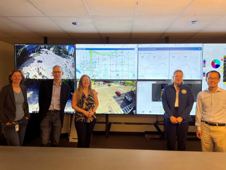 4.	Group of five staff members from the City of Houston and City of Bellevue standing in front of computer monitors showing footage of various roads and intersections and graphs