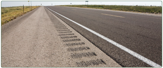 "A long, straight roadway in a rural area featuring rumble strips on the shoulders."