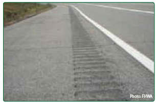 "A close up of asphalt with shoulder rumble strips milled into the surface."