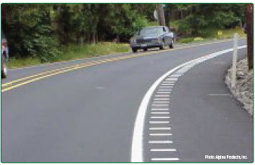 "A curving roadway with raised white strips on the shoulder just outside the travel lane that function as rumble strips."