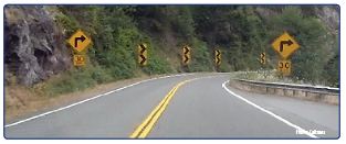 "US 199 in Del Norte County on the approach to a horizontal curve with curve warning signs, chevrons, and advisory speed placards. Photo courtesy of Caltrans."