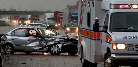 an ambulance and a totalled car in the breakdown lane of a highway heavy with traffic