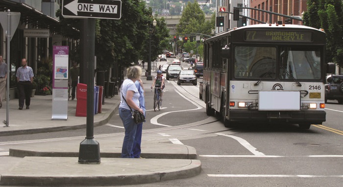 "Bus stop with crossing pedestrians in Portland, Ore. (Source: pedbikeimages.org/Laura Sandt) - two pedestrians waiting to cross an intersection by a bus stop"