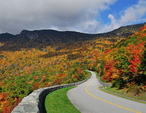 "a windy road through colorful autumnal forest-covered hills"