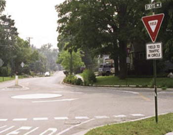 "Photo. A rural mini-roundabout. The roundabout consists has one travel lane and a flush concrete circle in the center."