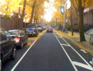 "Photo. A street where lane widths were reduced to provide exclusive space for cyclists. Through a reduction in lane width, the road currently has one on-street parking lane, one travel lane, and one bike lane. "