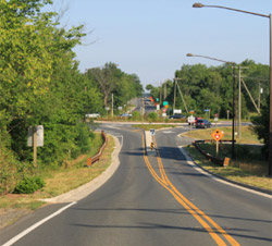 "Photo. A rural two lane road leading to a roundabout. "