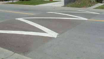 "Photo. A speed hump, which is a slightly raised section of roadway that is a couple of feet wide and has a zig zag white pavement marking on top. "