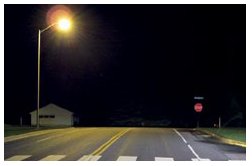 "Photo of a brighly lit luminaire above a stop-controlled intersection at night."