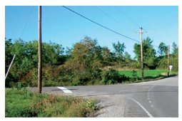 "Photo of a T intersection in a rural area with a brightly painted, easily visible stop bar on the stop approach."