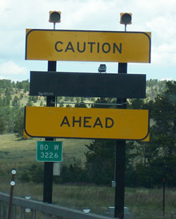 Photo of a warning sign with mounted warning lights displaying Caution, a changeable message panel, and Ahead.