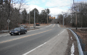 Photo of the eastbound approach to the intersection of Snake Hill Road and Chopmist Road showing a dark colored car driving by and you can see the traffic signal in the distance but you cannot see the stop bar.