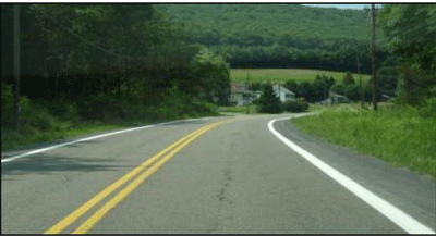 Photograph of a two-lane roadway in a rural area. An 8-inch edge line is installed on both sides within the curved section.