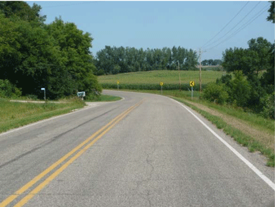 Photograph showing a two-lane roadway in a rural area with three chevron signs installed along the outside of the curve.