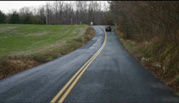 Photograph of a curve on a two-lane roadway in a rural area. Double solid center lines are installed along the curve for No Passing.