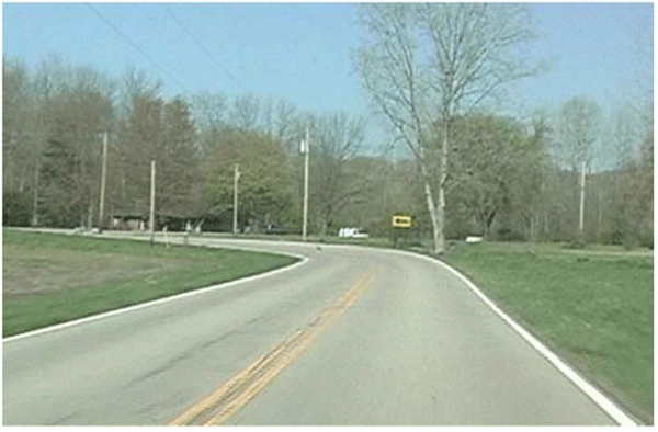 Photograph of a horizontal curve on a rural, two-lane road before signage updates. The curve has centerlines and edge lines, but only has one one-direction large arrow sign within the curve.