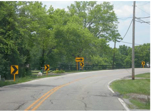 Photograph of the same horizontal curve as shown in Figure D-3 after signage updates. In addition to the existing one-direction large arrow sign, chevrons are installed on the outside of the curve.