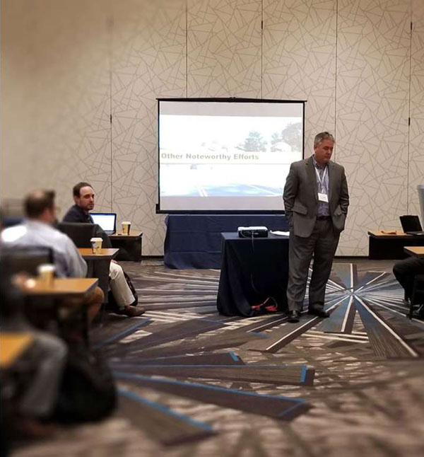 Photo of a Stakeholder meeting in Arlington, VA, in a conference room with a large screen display in the background.