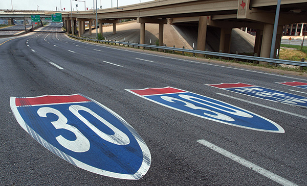 Figure 50. An picture of a section of freeway with route shield markings painted within the lanes.  The left two lanes have an I-30 shield, and the right two lanes have an I-35E shield.
