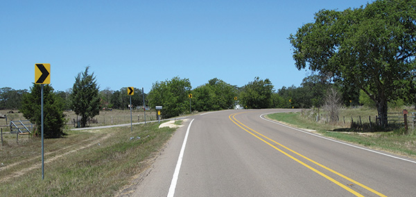 Figure 51. A picture of a horizontal curve to the right on a two-lane rural highway, with post-mounted chevrons on the left roadside, painted white edgelines, and raised pavement markers in the centerline.