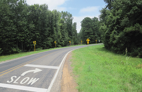 Figure 58. A picture of an approach to a horizontal curve on which the word 'SLOW', a right arrow, and two white transverse lines have been painted on the pavement surface.