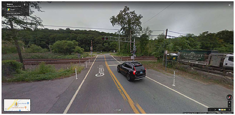 "Figure 18. Illustration of Use of Tubular Markers (Metro North Harlem Subdivision, Green Lane Crossing, Bedford Hills, NY ID 529898H) - This figure contains a photo of a highway-rail crossing showing a typical treatment of tubular markers along each side of the road being used in conjunction with edge lines. The photo shows an SUV approaching the highway-rail crossing."