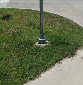 ""Figure 4.  Photo.  Example of breakaway hardware.  This photo shows the base of a sign pole on a street corner. The pole has breakaway hardware installed at the bottom.