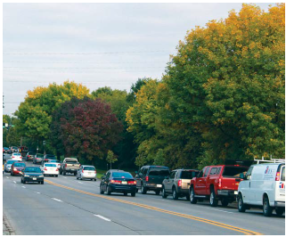 Four-lane undivided roadway with through vehicles backing up in the right travel lane to avoid being stopped behind left-turning traffic stopped at an intersection ahead.