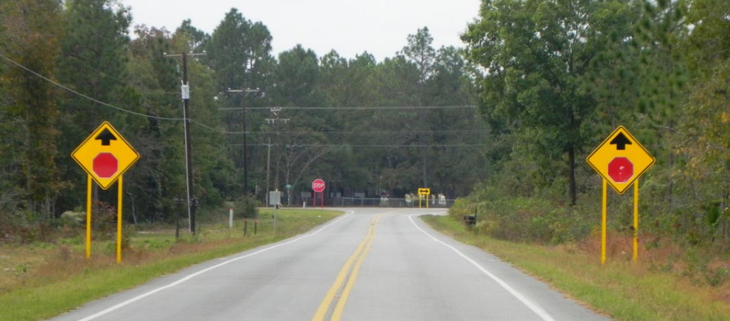 "Countermeasures present on the minor leg of a T-intersection. On both sides of the roadway, W3-1 Stop Ahead warning signs are present. Each W3-1 sign is supported by two metal posts covered in yellow reflective material."