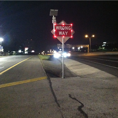 "This photo depicts an LED-illuminated Wrong Way sign with a radar detector mounted to the sign. The sign is illuminated by bright red bulbs around the edges."