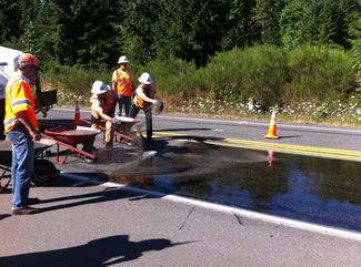 "Road workers apply a surface treatment to a roadway."