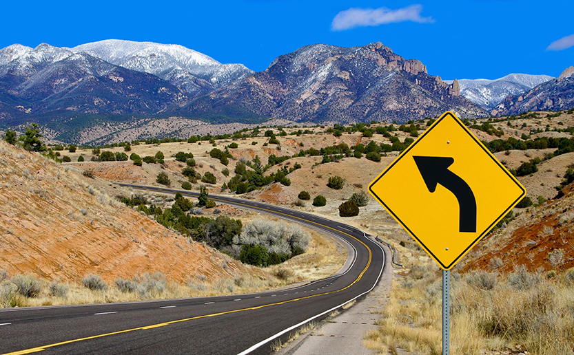 image of a highway curve with a warning sign