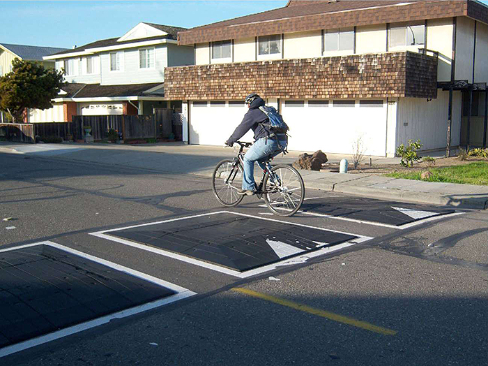 Figure 6.2. Bicyclist Passing Through Speed Cushion. This figure contains a photograph of a bicyclist passing through a speed cushion in a residential neighborhood. Sidewalk and houses are in the background.