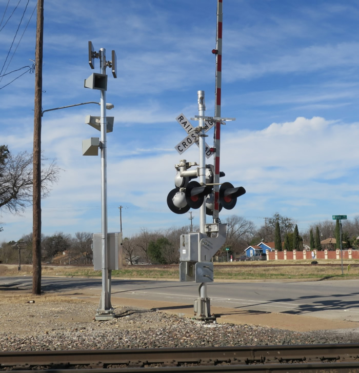 "Figure 26. Automated Wayside Horn - This figure shows a photograph of an automated wayside horn and a crossing gate. In this photograph, the automated wayside horn three horns in different directions to alert road users traveling from each of these directions."