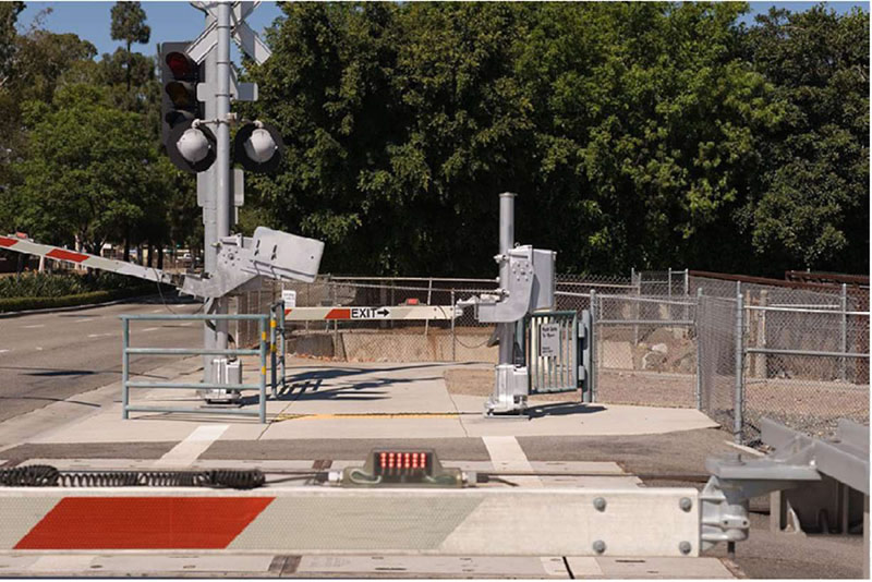 "Figure 56. Illustrative Example of Pedestrian Automatic Gate with Swing Gate - This figure is a photograph of a pedestrian automatic gate with a swing gate with exit signs to also act as an emergency exit for users within the crossing. There is no train in the photograph at this crossing."