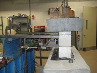 Figure 5. This is a photo showing a side view of frictional connectional testing. Concrete masonry units are stacked with a layer of geotextile sandwiched in between and attached to a clamp that is attached to a worm gear. Dead weight and lead ingots are placed on top of the concrete masonry units.