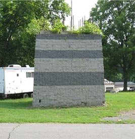 Figure 14. This is a photo showing a tested geosynthetic reinforced soil pier. Vegetation is growing out from the top. A trailer and trees are shown in the background.