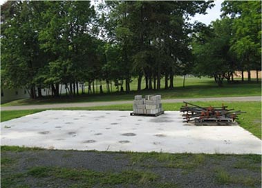 Figure 17. This is a photo showing the outdoor concrete strong floor. A pallet of concrete masonry units and some helical anchors lie on top.