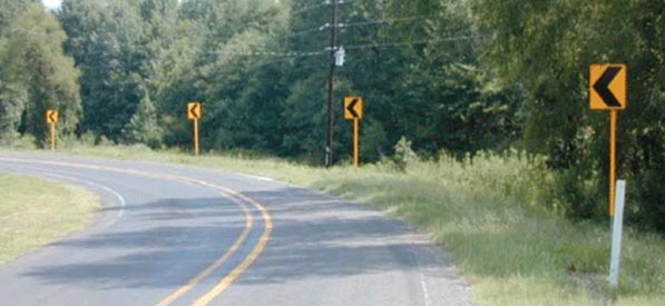 "A two-lane undivided roadway bearing to the left. On the outside of the curve, to the right, is a clear grassy area least 20 feet in width, featuring a gentle foreslope and steeper backslope."