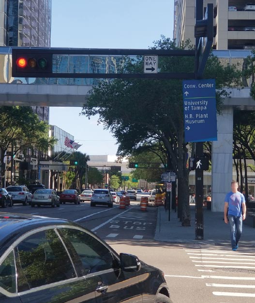 "A pedestrian establishing a presence in the crosswalk during the Leading Pedestrian Interval. A pedestrian signal on the far side of the crosswalk indicates the WALK phase, while the accompanying overhead traffic signal shows RED. The right turning vehicle would otherwise conflict with the crosswalk.""