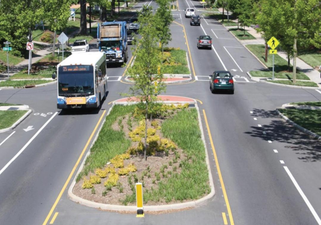 "alt="Photo: This photograph, taken above the median of a two-lane divided roadway, demonstrated the use of pedestrian and refuge islands. The roadway features crosswalks, pedestrian warning signs, and bike lanes. Traffic calming techniques, such as on street parking and extended curbs, are also present.""