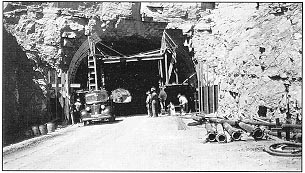 Looking west at one of the first phases of construction on the Alamogordo-Cloudcraft Forest Highway Project. Erecting footing formwork and reinforcing steel at east portal. Engineers cross-sectioning inside tunnel.