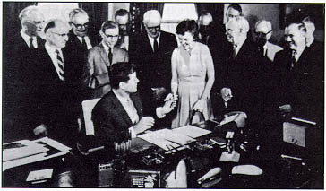 President John F. Kennedy during signing ceremony for the Federal Aid Highway Act of 1961. From left to right: House Majority Leader John W. McCormack (MA); Senator Francis Case (SD); Senator Pat McNamara (MI); Senator Dennis Chavez (NM); Representative John A. Blatnik (MN); Representative George H. Fallon (MD); Senator Maureen B. Newberger (OR), who received one of the pens used by the President; Treasury Secretary Douglas Dillon; Under Secretary for Transportation Clarence D. Martin, Jr.; Secretary of Commerce Luther Hodges; Representative James C. Auchincloss (NJ); Representative William C. Cramer (FL); and Administrator Rex Whitton behind Representative Cramer.