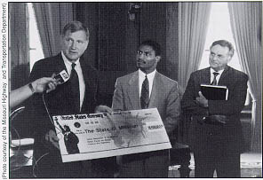 After receiving a symbolic check for $28.5 million in emergency relief funds from Administrator Rodney E. Slater (center), Missouri Governor Mel Carnahan (left) talks with reporters. Chief Engineer Wayne Muri of the Missouri Highway and Transportation Department looks on.